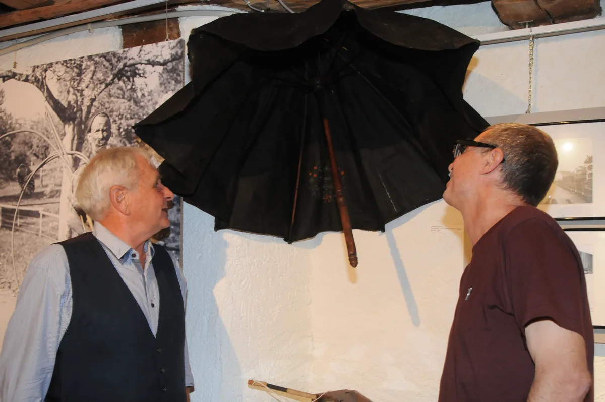 Mark Plüss (links) und Markus Brühlmeier mit dem geschichtsträchtigen Schirm. Man sieht zwei Männer, die einen alten Schirm im Museum betrachten.